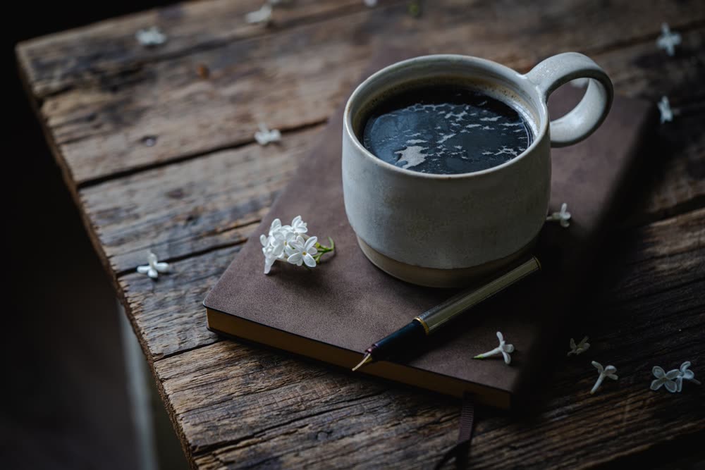 A cup of coffee on a notebook with a pen, on an old wooden table